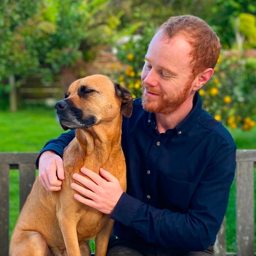 Chris Barlow sitting on a garden bench with his arm around a tan dog